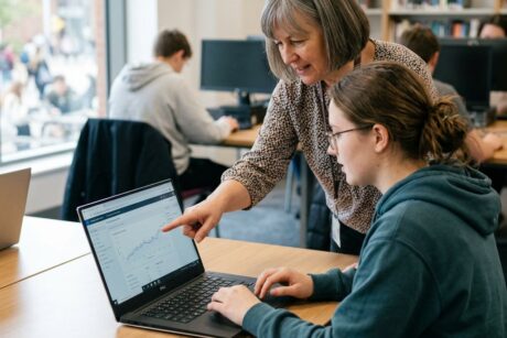 Teacher pointing at line graph on student's laptop while explaining